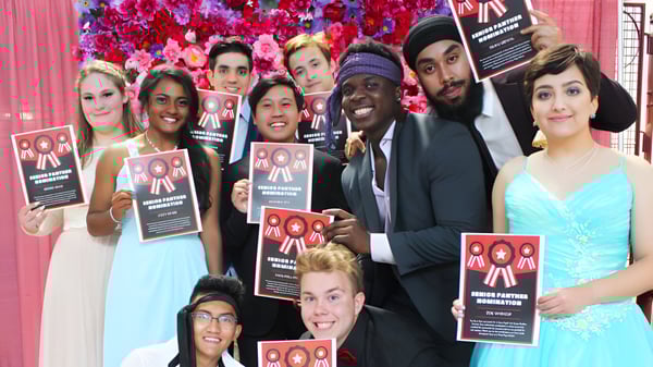 Schüler der J. Percy Page High School halten Schilder für Einwanderungsreform vor einem farbenfrohen Blumenhintergrund.