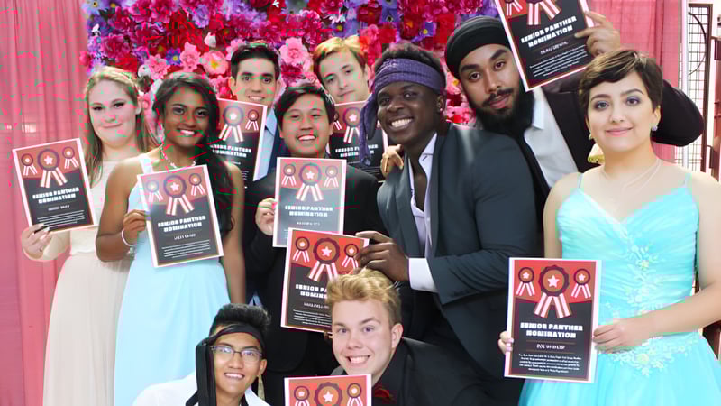 Schüler der J. Percy Page High School halten Schilder für Einwanderungsreform vor einem farbenfrohen Blumenhintergrund.