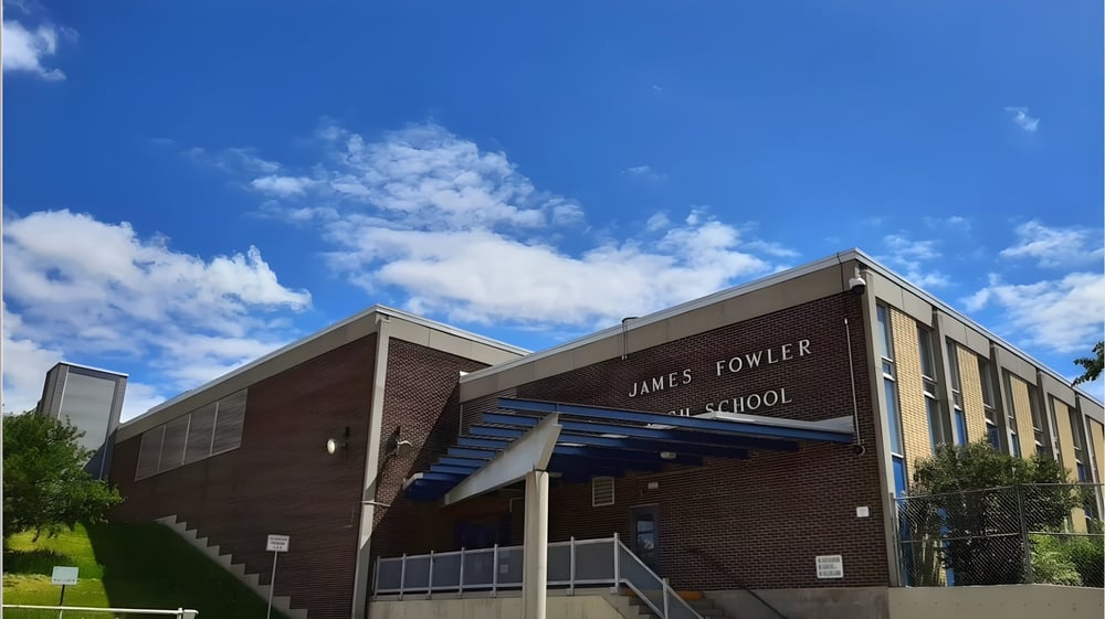 Das Backsteingebäude der James Fowler High School steht vor einem blauen Himmel mit weißen Wolken.