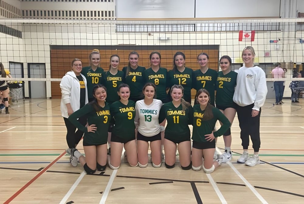Eine Gruppe weiblicher Volleyballspielerinnen in grünen Trikots posiert auf dem Volleyballfeld der James M. Hill Memorial High School.