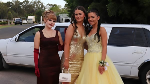 Drei Schülerinnen der James Nash State High School stehen in formeller Kleidung vor einem weißen Fahrzeug im Außenbereich der Schule.