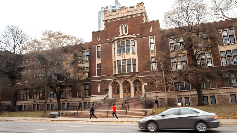 Das große Backsteingebäude mit prominentem Turm gehört zum Jarvis Collegiate Institute und wird von Bäumen umgeben.