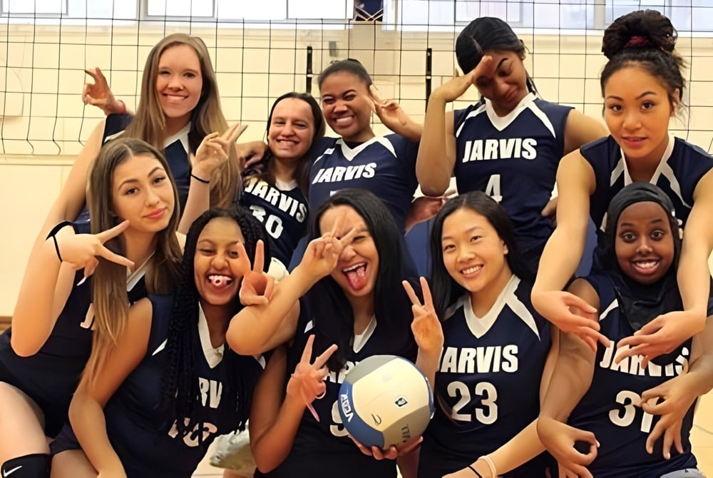 Eine Gruppe jungen Schülerinnen des Jarvis Collegiate Institute in Sportuniformen posiert gemeinsam in einem Sportgebäude.