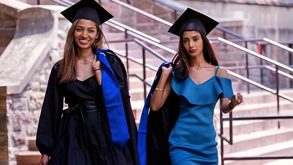 Zwei Schülerinnen in Abschlusskleidung posieren auf einer Treppe vor einem Backsteingebäude auf dem Campus des Jarvis Collegiate Institute.