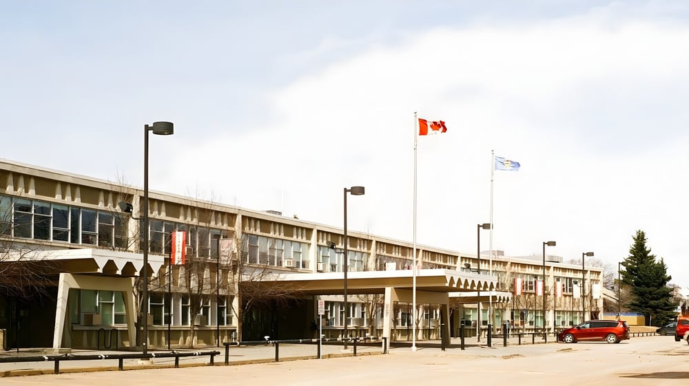 Das mehrstöckige Gebäude der Jasper Place High School mit einer Reihe von Flaggen im Vordergrund und einem Parkplatz sowie Bäumen im Hintergrund.