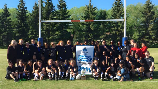Eine Gruppe von Schülerinnen und Schülern der Jasper Place High School posiert auf einem Rasenfeld vor Kiefern.