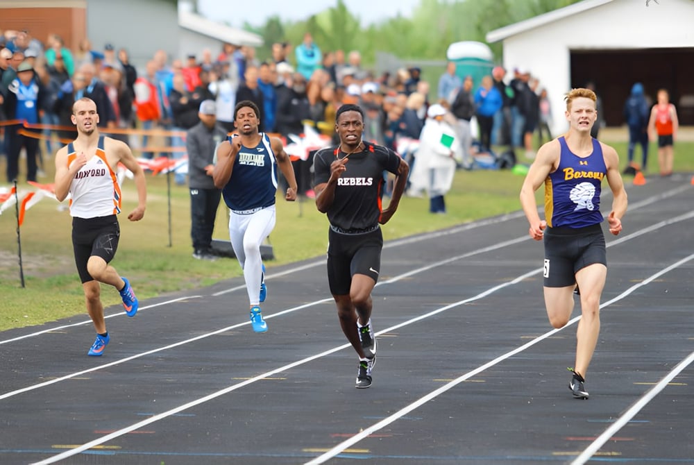 Schüler der Jasper Place High School laufen im Wettkampf auf der Laufbahn mit Zuschauern und Schulgebäuden im Hintergrund.