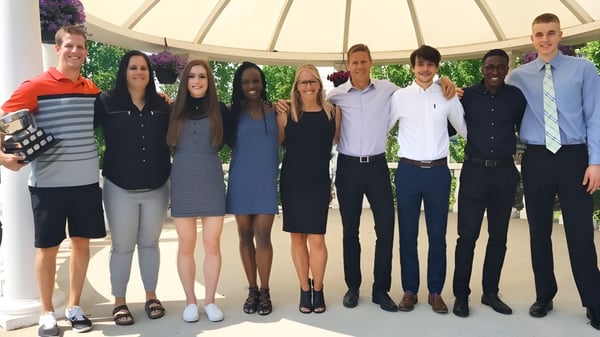 Eine Gruppe von Schülerinnen und Schülern steht im Kreis vor einem grünen Hintergrund auf dem Campus der Jasper Place High School.