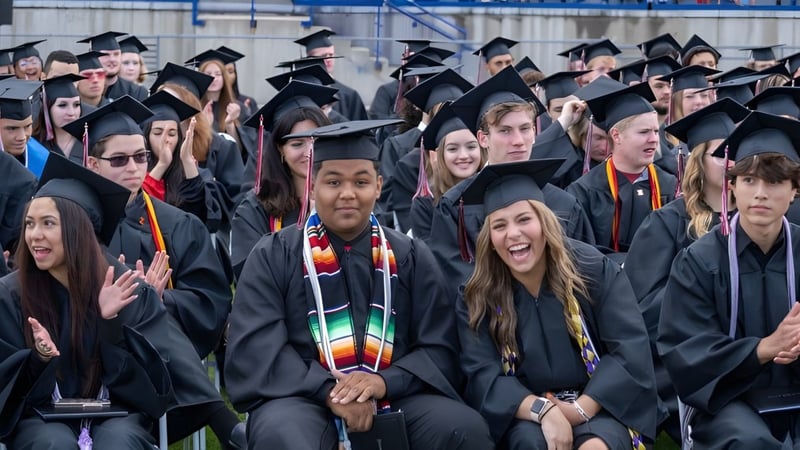 Eine große Gruppe von Absolventen in schwarzen Talaren und Hüten bei der Abschlussfeier der Jeffco Public Schools im Freien.