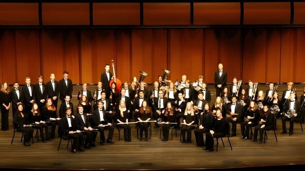 Ein großes Orchester der Jenison Public Schools tritt auf einer Bühne mit hölzerner Rückwand und Zuschauerreihen im Hintergrund auf.