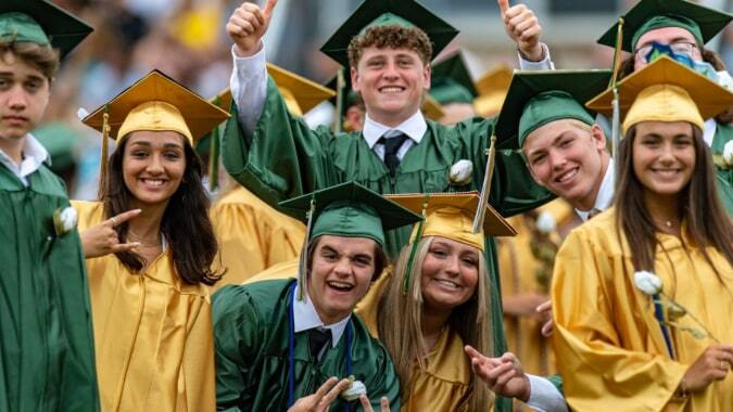 Eine Gruppe von Absolventen der Jesus and Mary Secondary School feiert im Freien in grünen und goldenen Abschlussroben.