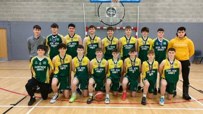 Eine Gruppe von Schülern der Jesus and Mary Secondary School posiert gemeinsam auf dem Basketballfeld vor einem Korb.