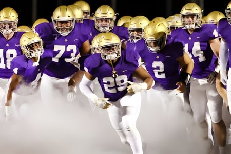 Eine Gruppe von Fußballspielern in lila Uniformen steht am Abend auf dem Spielfeld der John Bapst Memorial High School.
