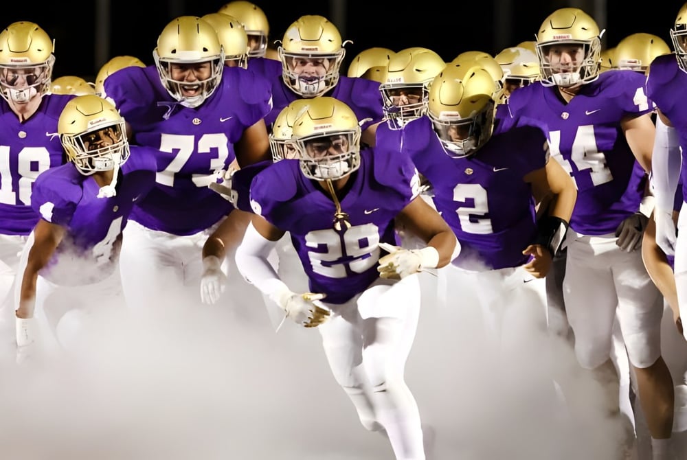 Eine Gruppe von Fußballspielern in lila Uniformen steht am Abend auf dem Spielfeld der John Bapst Memorial High School.