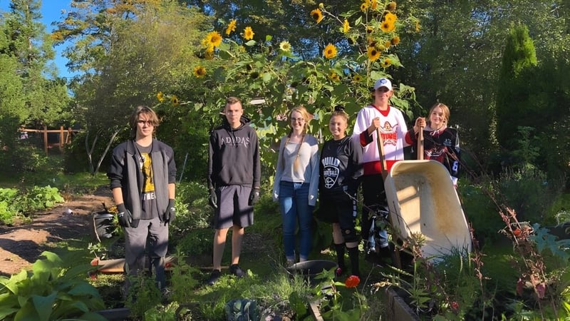 Eine Gruppe von Personen steht in einem bunten Garten mit Bäumen und einer Steinskulptur auf dem Gelände der John Barsby Secondary School.