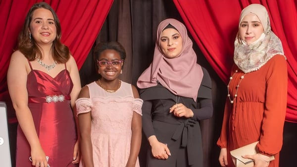 Vier Schülerinnen in bunten Kleidern und Hijabs stehen vor einem roten Vorhang auf dem Gelände der John Barsby Secondary School.