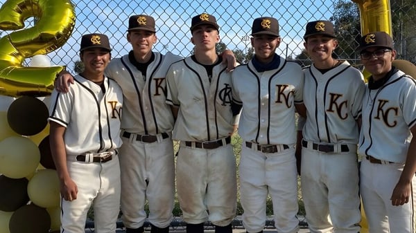 Eine Gruppe junger Baseballspieler steht vor einem Maschendrahtzaun auf dem Gelände der John F. Kennedy High School.
