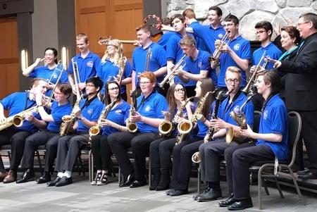 Schüler der John Maland High School in blauen Uniformen bei einer Orchesterprobe vor einem Steingebäude.