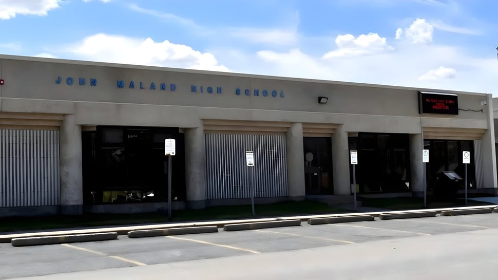Das große graue Schulgebäude der John Mallard High School ist mit ihrem Namen an der Fassade deutlich zu erkennen.