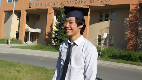 Ein Schüler der John McCrae Secondary School steht in Talar und Barett vor dem Schulgebäude.