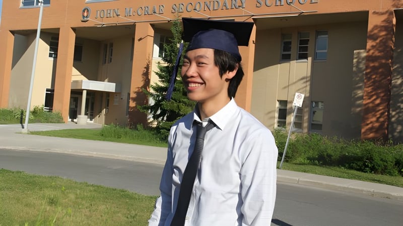 Ein Schüler der John McCrae Secondary School steht in Talar und Barett vor dem Schulgebäude.