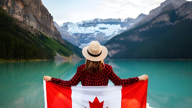 Eine Person steht vor einem türkisfarbenen See mit schneebedeckten Bergen auf dem Gelände der John McCrae Secondary School.