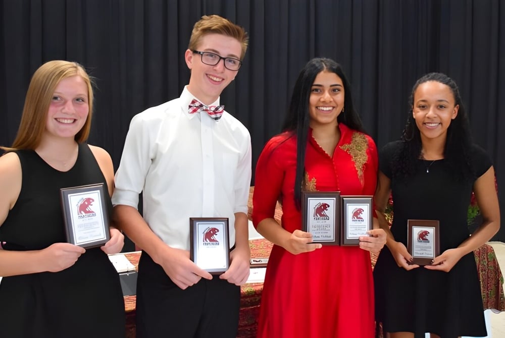 Vier Personen halten während einer Preisverleihung auf der John McGregor Secondary School Auszeichnungen in der Hand.