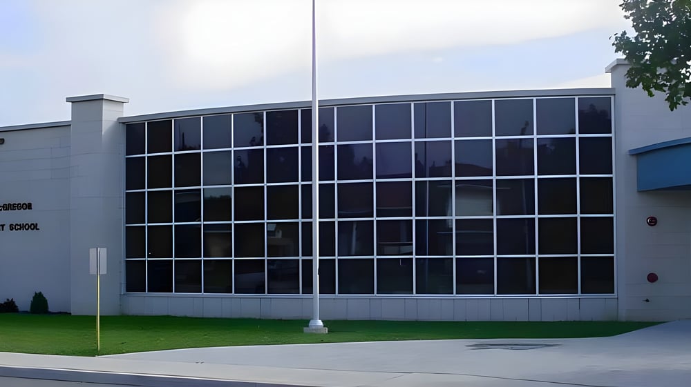 Das moderne mehrstöckige Gebäude der John McGregor Secondary School steht auf einer begrünten Fläche mit Bäumen.