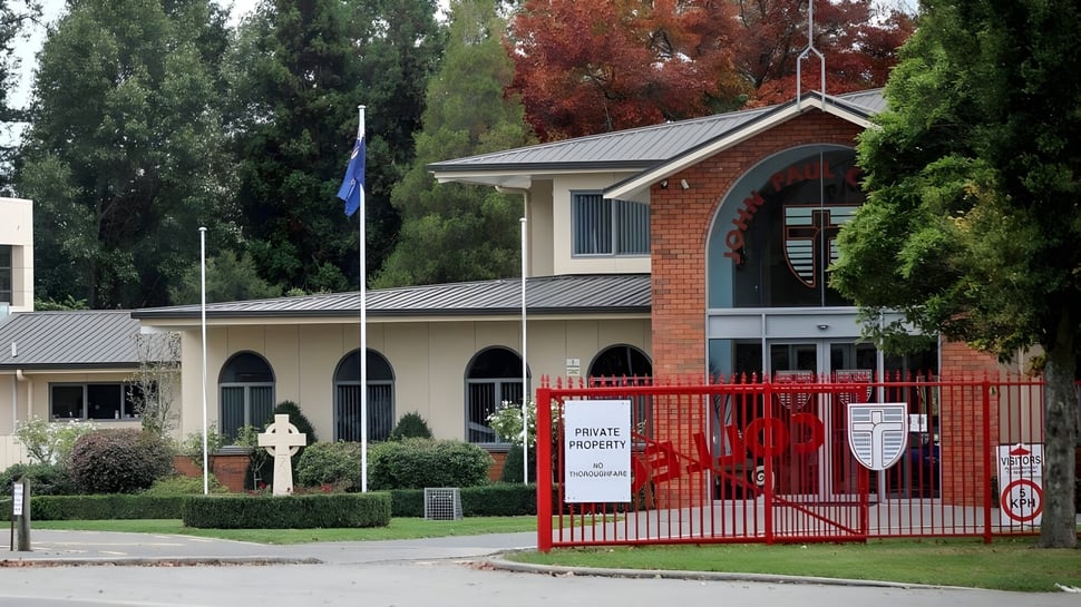 Das Backsteingebäude mit rotem Tor des John Paul College ist von Bäumen und Grünflächen umgeben.