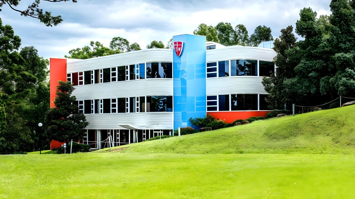 Das moderne und farbenfrohe Gebäude des John Paul College steht auf einem grasbewachsenen Hang und ist von Bäumen umgeben.