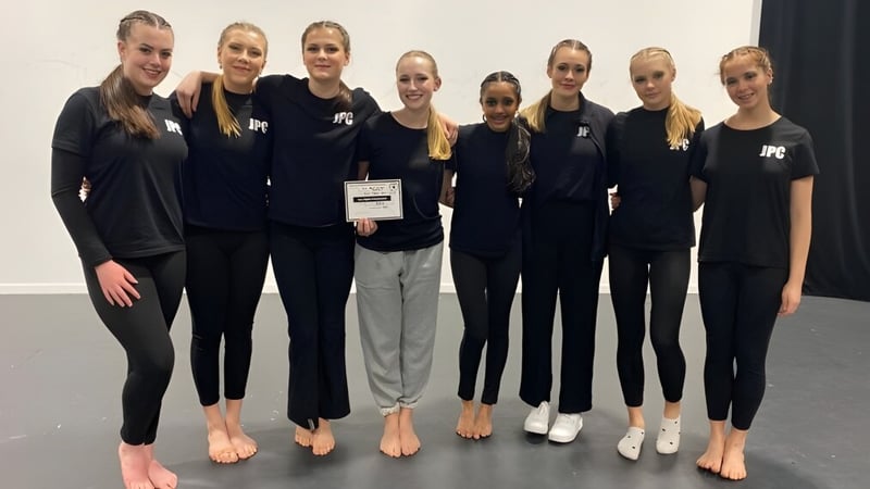 Eine Gruppe Schülerinnen des John Paul College trägt schwarze Uniformen und posiert gemeinsam in einem Studio.