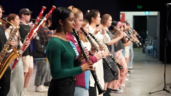 Schülerinnen und Schüler des John Paul College spielen auf der Bühne Windinstrumente in einem Orchester.