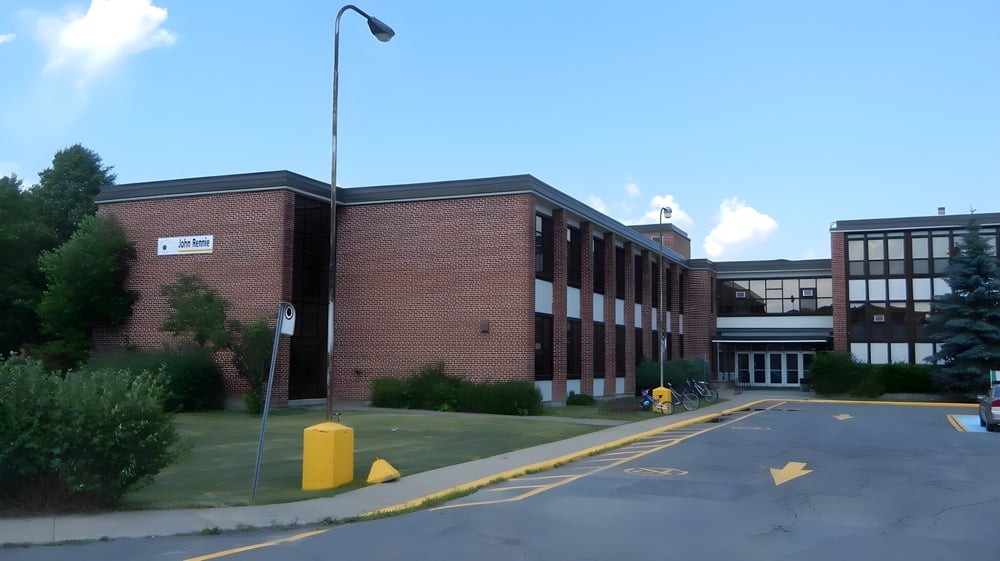 Das Backsteingebäude der John Rennie High School ist von Grünflächen umgeben und unter einem klaren blauen Himmel zu sehen.