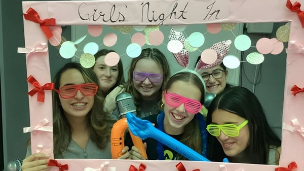 Eine Gruppe Schülerinnen der John Rennie High School posiert vor einem Banner mit der Aufschrift Girls Night In in festlicher Dekoration.