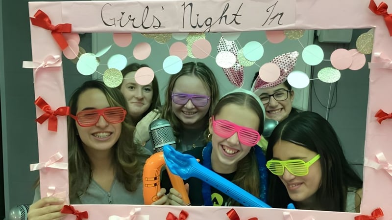 Eine Gruppe Schülerinnen der John Rennie High School posiert vor einem Banner mit der Aufschrift Girls Night In in festlicher Dekoration.