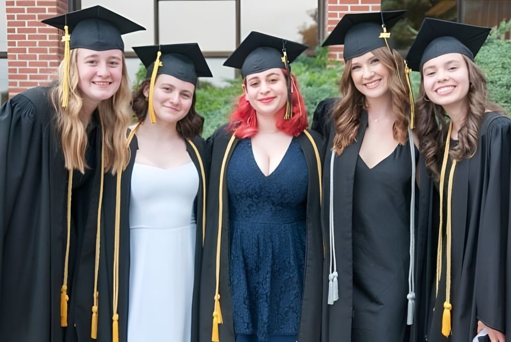 Fünf Absolventinnen der John Rennie High School stehen vor einem Backsteingebäude und feiern ihren Abschluss.