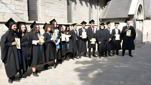 Eine Gruppe von Absolventinnen und Absolventen der John Scottus Secondary School steht in akademischer Kleidung vor einem Steingebäude.