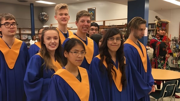 Eine Gruppe von Schülern des John Taylor Collegiate posiert in ihren Abschlussgewändern in einem Klassenraum.