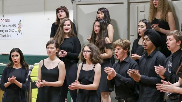 Eine Gruppe von Schülerinnen und Schülern steht in einem Raum mit einem Schild an der Wand auf dem Campus der John Taylor Collegiate.