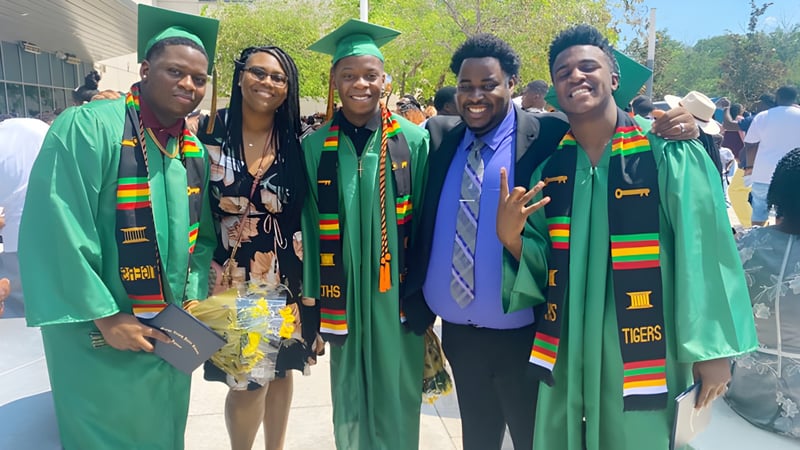 Eine Gruppe von Schülern der Jones High School posiert draußen in bunten Abschlussroben vor einem Gebäude und Bäumen.