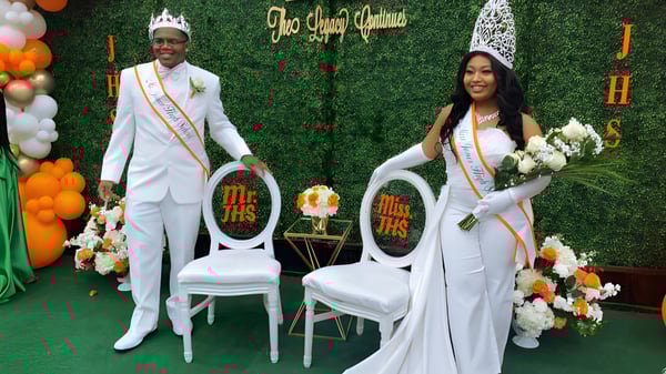 Ein Mann und eine Frau in formeller Kleidung stehen bei einer Veranstaltung auf dem Campus der Jones High School vor einem dekorativen Hintergrund mit Blumen und Luftballons.
