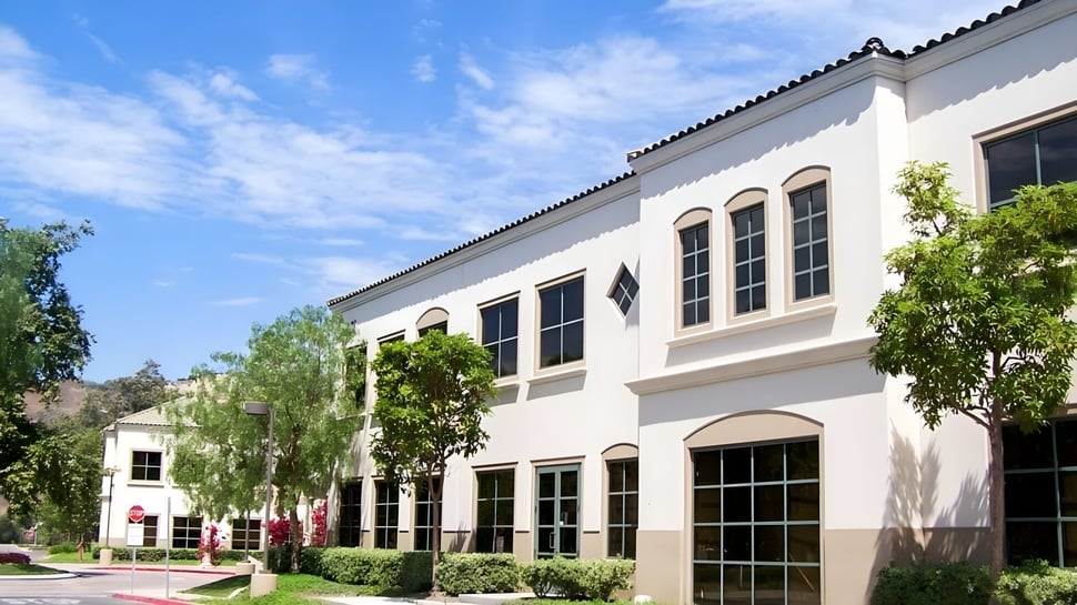 Das mehrstöckige Gebäude mit Bogenfenstern und Ziegeldach auf dem Campus der JSerra Catholic High School ist von grüner Vegetation umgeben.