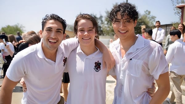 Drei Schüler der JSerra Catholic High School stehen lächelnd im Freien vor Bäumen und anderen Personen.