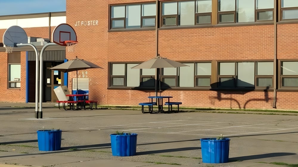 Das Backsteingebäude der J.T. Foster High School mit Basketballkorb und mehreren blauen Mülltonnen auf dem Vorplatz.