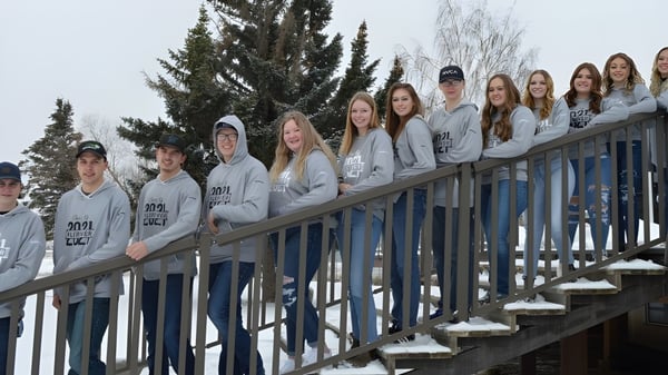 Schüler der J.T. Foster High School stehen auf einem Holzbalkon mit verschneiten Bäumen im Hintergrund.