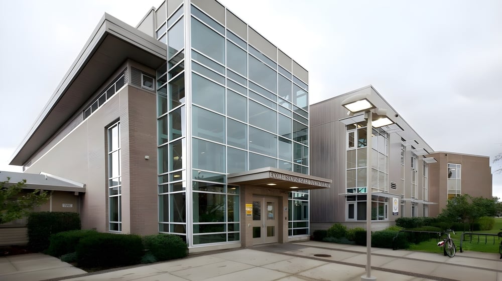 Das moderne mehrstöckige Gebäude mit Glasfassade der Jules Verne School Vancouver ist von einem gepflasterten Weg und Grünflächen umgeben.