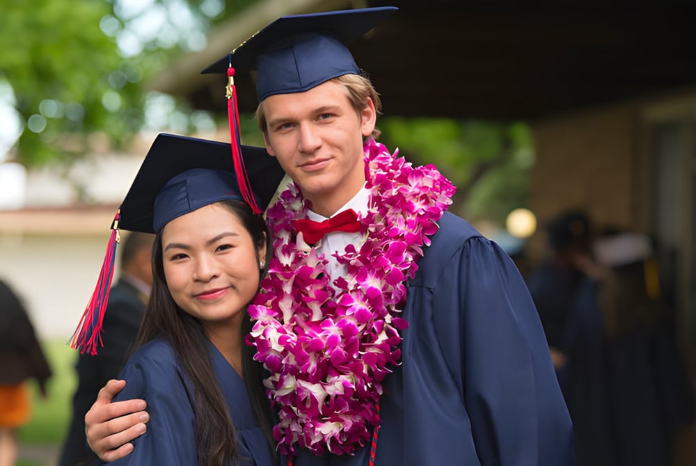 Zwei Absolventen in Abschlusskappen und -roben stehen gemeinsam auf dem Campus der Justin Siena High School.