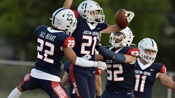 Eine Gruppe von Footballspielern der Justin Siena High School spielen auf einem Rasenfeld unter blauem Himmel.