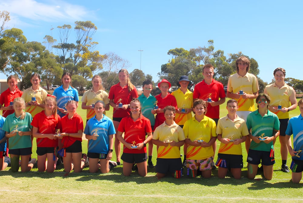 Eine Gruppe Schüler der Kadina Memorial School steht auf dem Sportfeld auf einer Wiese vor Bäumen unter klarem Himmel.