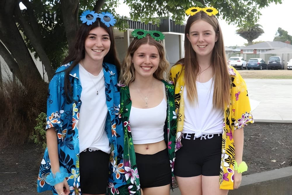 Drei Schülerinnen der Kaiapoi High School posieren lachend draußen vor Bäumen und Gebäuden.